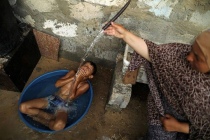 Una donna palestinese fa il bagno a suo figlio con acqua di un serbatoio riempito da una'associazione umanitaria